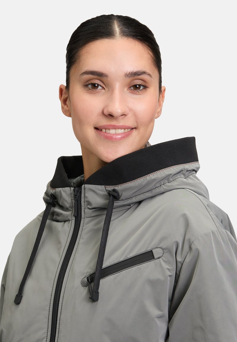 Graue gepolsterte Jacke mit schwarzen Akzenten, Reißverschluss-Brusttasche, verstellbarem Kordelzug an der Kapuze und glatter, glänzender Textur.