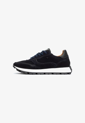 Marineblauwe suède sneaker met contrasterende witte rubberen zool, zwarte accenten en blauwe veters. Heeft een lage profiel en textuurdetails op het oppervlak.