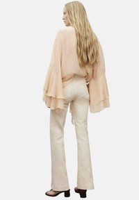 Peach bell-sleeve top with layered ruffles paired with light beige flared jeans, set against a plain white background.