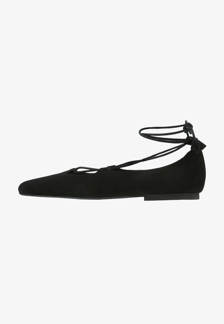 Ballerine plate en daim noir avec bout pointu et lacets autour de la cheville noués à l'arrière.