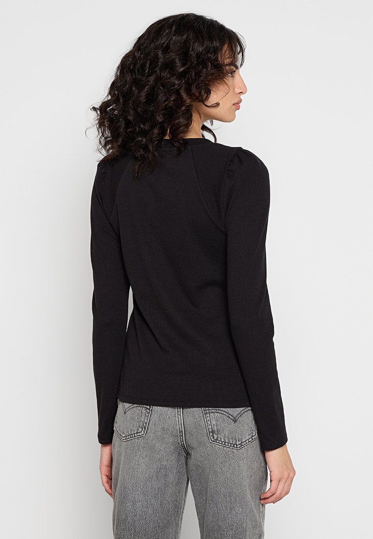 Czarny top z długim rękawem, z delikatnymi falbankami na ramionach, dopasowany fason i miękka tekstura, w połączeniu z jasnoszarymi spodniami z wysokim stanem.