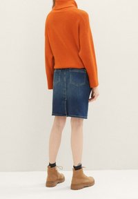 Oranžový žebrovaný svetr s vysokým límcem, ve spojení s džínovou tužkovou sukní. Modelka má na sobě béžové kotníkové boty. Textura je patrná v pletenině a džínech.