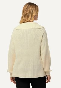 Maglione lavorato a maglia color crema con colletto ampio, texture a costine e vestibilità morbida. Le maniche lunghe si stringono ai polsini, con un orlo posteriore dritto.