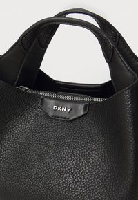 Svart skinnhåndveske med strukturert overflate, med to håndtak, glidelås og metalllogo.