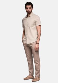 Lichtbeige shirt met korte mouwen en een zak, gecombineerd met tan broek en tan moccasins. Glad textuur en een op maat gemaakte pasvorm.