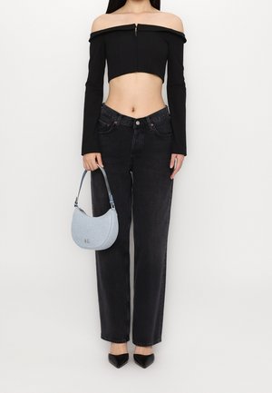 Femme portant un crop top noir à épaules dénudées, un jean noir taille haute, des chaussures noires pointues, tenant un sac à main bleu clair avec une bandoulière.