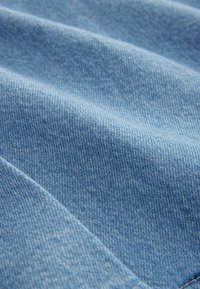 Gros plan sur un tissu en denim bleu clair montrant la texture et un motif de tissage diagonal avec des plis doux.