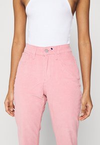 Różowe spodnie corduroy z wysokim stanem, wyposażone w przednie kieszenie, metalowy guzik oraz delikatną teksturę prążkową.