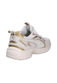 Scarpa sportiva bianca con accenti dorati, caratterizzata da una tomaia texturizzata, colletto imbottito e una suola in gomma spessa con scanalature. Logo visibile sul lato.