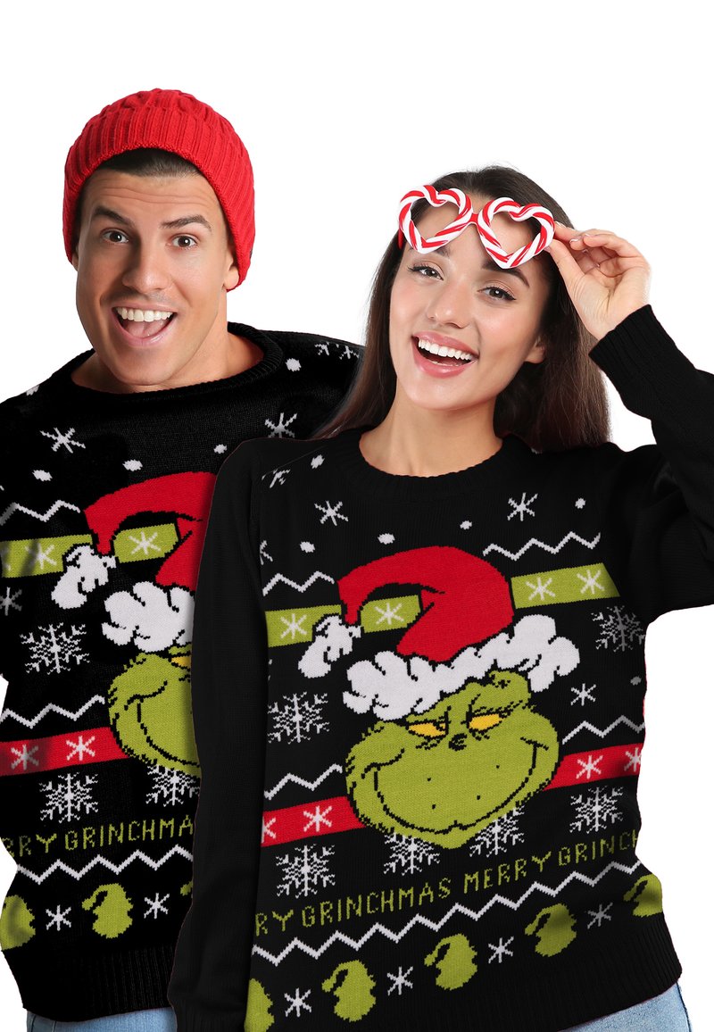 A smiling man and woman wear matching Grinch Christmas sweaters; woman holds heart-shaped candy cane glasses near her eyes.