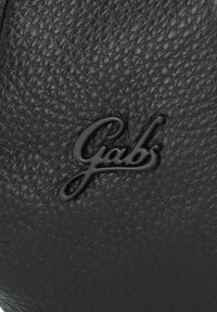 Superficie de cuero negro texturizado con un logo de Gabs en relieve en un color negro a juego, creando un detalle de diseño sutil.