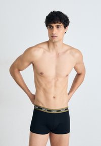Schwarze Boxershorts mit einem weichen, elastischen Bund, der das Logo "HUGO" in Weiß auf einem olivgrünen Hintergrund zeigt. Glatter Stoff.