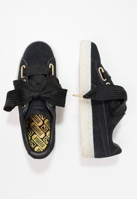 Baskets en daim noir avec de larges lacets tissés noirs, œillets dorés et une semelle blanche texturée, dotées d'une semelle intérieure jaune à motifs.