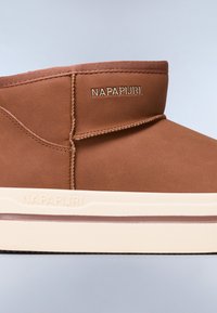 Botas de tobillo marrones con un acabado suave y mate, con forma redondeada y costuras sutiles, con la marca "NAPAPURI" en dorado en el lateral.