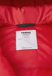 Interno di giacca rossa con tessuto liscio e isolante. Include un'etichetta bianca con il nome del marchio, la taglia e linee per la personalizzazione.