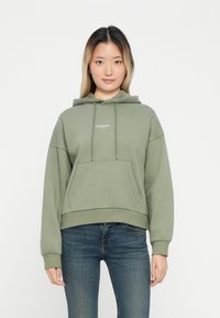 Olijfgroene hoodie met trekkoorden, voorzak en wit logo in het midden van de borst. Zachte stof, relaxed fit, lange mouwen en ribgebreide zoom.