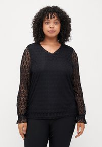 Μαύρη μπλούζα με μακριά μανίκια και V λαιμόκοψη, με διακοσμημένα μανίκια από δαντέλα και υφή στο σώμα. Το υλικό είναι ελαφρύ και ρέον.