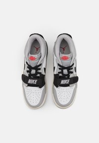 Tenisky Nike s šedým a bílým koženým svrškem, černými akcenty, výrazným černým páskem a červeným logem na jazyku a patě.