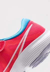 Różowy but sportowy z teksturowaną cholewką, niebieskimi akcentami i białą podeszwą. Posiada zakrzywioną konstrukcję z wyraźnym białym wzorem w paski.