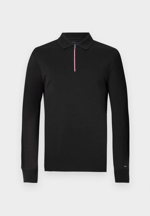 Sort langærmet polo skjorte med lynlås ved halsen. Har en kontrasterende stribe i rød, hvid og blå på lynlåsen. Glat, blødt stof.