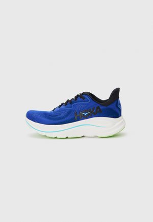 Zapatilla de running azul con parte superior de malla, una suela intermedia blanca gruesa con acentos verdes, cordones negros y un logo de HOKA en el costado.