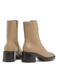 Beżowe skórzane botki za kostkę z kwadratowym noskiem, sznurowanym przodem i zamkiem bocznym. Charakteryzują się masywnym czarnym obcasem i gładką teksturą.