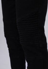 Jeans negros con paneles acanalados en los muslos y las rodillas. La tela tiene una textura suave y un diseño de corte ajustado.