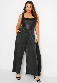 Svart ärmlös bodysuit i kombination med vida glittriga svarta byxor med strukturerad väv och sidofickor. Svarta klackar fulländar looken.