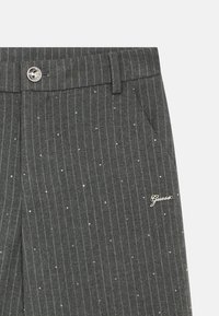 Γκρι παντελόνι με λεπτές ρίγες, ασημένιες τρουκς, καλοραμμένη μέση και μικρό λογότυπο "Guess" στο πλάι, με πλαϊνές τσέπες και ομαλή υφή.