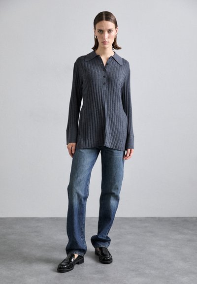 Camisa cinza de manga longa com nervuras e placket de botões, combinada com jeans azuis de perna reta e mocassins pretos. Texturas suaves em todo o conjunto.