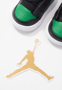 Černé a zelené tenisky s bílou podrážkou nad zlatým logem Jumpman na bílém pozadí.