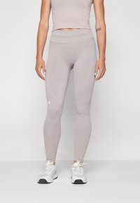 Világosszürke Under Armour leggings, magas derékkal, varrásmentes kialakítással és textúrázott anyaggal. Fehér sportcipővel párosítva.