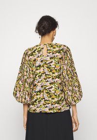 Blusa floral com mangas bufantes, apresentando um fundo verde escuro e um padrão floral multicolorido. Detalhe nas costas em forma de chave.