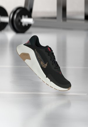 Μαύρο και μπεζ αθλητικό παπούτσι Nike με μοτίβο λεοπάρδαλης στη φιγούρα Swoosh, που αιωρείται πάνω από το πάτωμα ενός γυμναστηρίου· θολές αλτήρες στο φόντο.