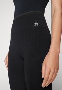 Fekete, bordázott leggings magas derékkal, diszkrét logóval és textúrált anyaggal. Simára szabott, testhez álló fazon.