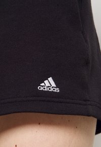 Svarta träningsshorts i mjukt tyg, med en vit broderad Adidas-logotyp nära fållen och en ren, minimalistisk design.