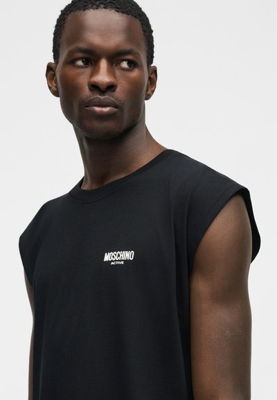 Άνδρας που φορά μαύρο αμάνικο πουκάμισο Moschino Active, κοιτάζει προς τα πλάγια με φόντο απλό και φωτεινό.