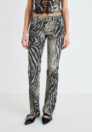 Jeans de mezclilla con estampado de cebra que presentan un corte slim, cintura alta y una textura desgastada en tonos negro y beige, combinados con zapatos negros de punta.