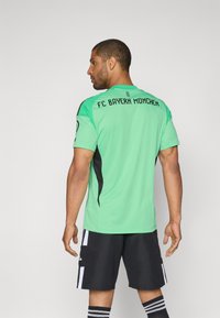Vihreä FC Bayern Münchenin maalivahdin paita lyhyillä hihoilla, mustat yksityiskohdat ja logo selässä, yhdistettynä mustiin shortseihin ja raidallisiin sukkiin.