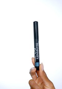Marqueur cylindrique noir avec un accent bleu à la base, portant le texte "À L'INFINI". Tenue entre des doigts sur un fond blanc.