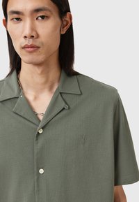 Olivenfarget kortermet skjorte med krage, med et subtilt broderi-design og lyse knapper, laget av et glatt stoff.