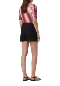 Gestreepte rode en witte top met korte mouwen, gecombineerd met zwarte shorts met een relaxed fit en een elastische tailleband, afgemaakt met platte zwarte sandalen.