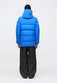 Blue puffer jacket with a hood, featuring horizontal quilting and a relaxed fit, paired with loose, dark cargo pants with large pockets.