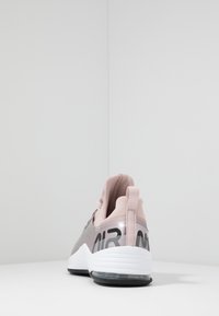 Achteraanzicht van een enkele roze sport sneaker met een witte zool en zwarte "AIR" tekst, geplaatst op een witte ondergrond tegen een effen witte achtergrond.