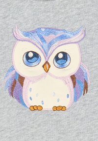Broderat ugglemotiv på grått tyg, med blå och lila fjädrar, stora blå ögon och bruna detaljer. Cirkulär form med dekoration.