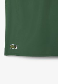 Polo vert en tissu coton doux. Présente un petit logo de crocodile brodé en blanc, situé au niveau de l'ourlet inférieur.