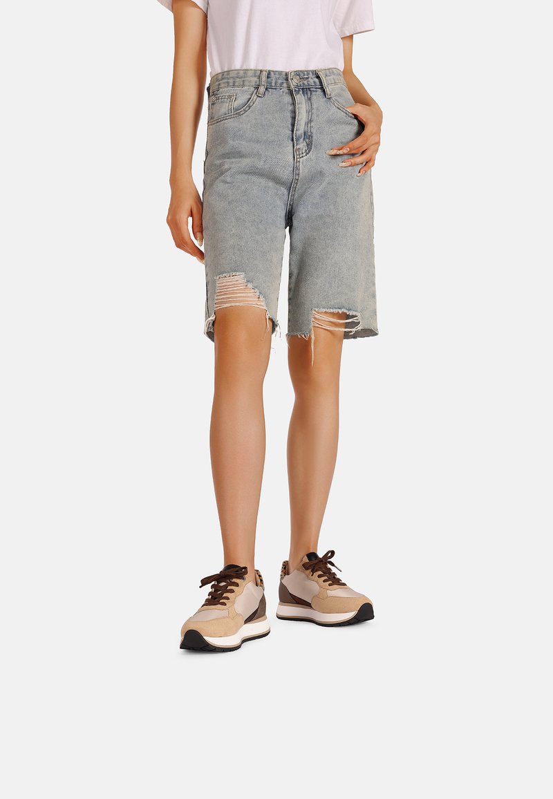 Shorts in denim blu chiaro con orlo sfilacciato e dettagli strappati. Abbinati a sneakers beige e marrone, che enfatizzano un look informale.