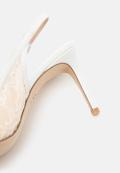 Chaussure blanche à talon haut avec bride arrière, superposition de dentelle beige et semelle marron clair, montrée de profil sur fond uni.