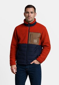 Rode fleecejas met een marineblauwe ondersectie en een bruine borstzak. Voorzien van een hoge kraag en een rits sluiting. Casual ontwerp en een gestructureerde stof.