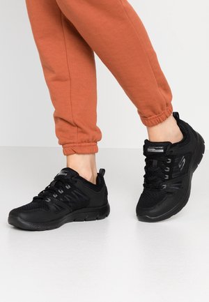 Zwarte sportschoenen met een bovenwerk van mesh en synthetisch materiaal, een gestructureerd patroon en vetersluiting. Gecombineerd met oranje sweatpants tot de enkels met omslag.